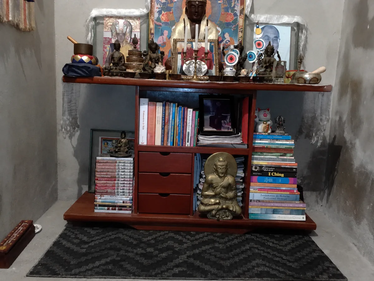 O primeiro altar, sobre um móvel de madeira em uma parede de cimento, com livros, imagens e taças de oferenda